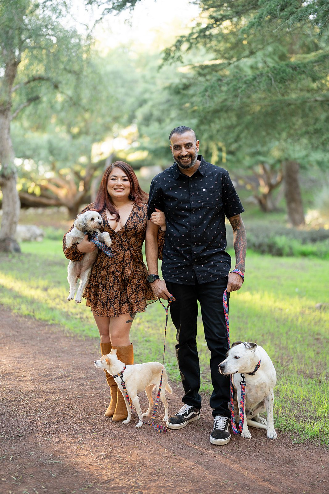 Photographer Dipan Desai and his partner posing for a lifestyle family portrait in a wooded park with their three dogs.